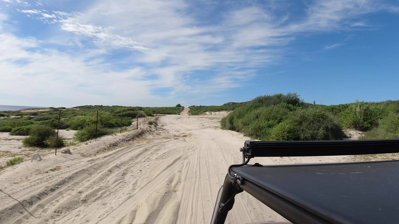 Sandy desert road ahead with vehicle roof and light bar in foreground.