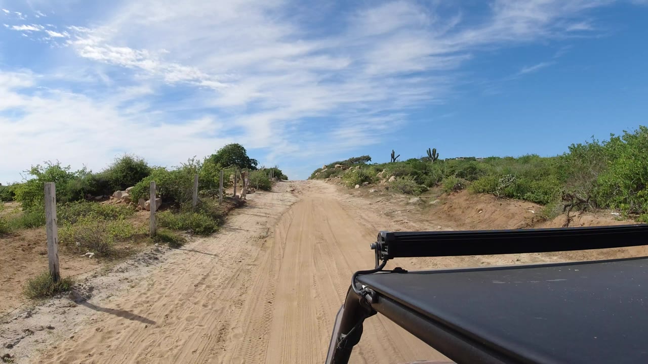Dusty road ahead with scrub and vehicle edge in foreground.