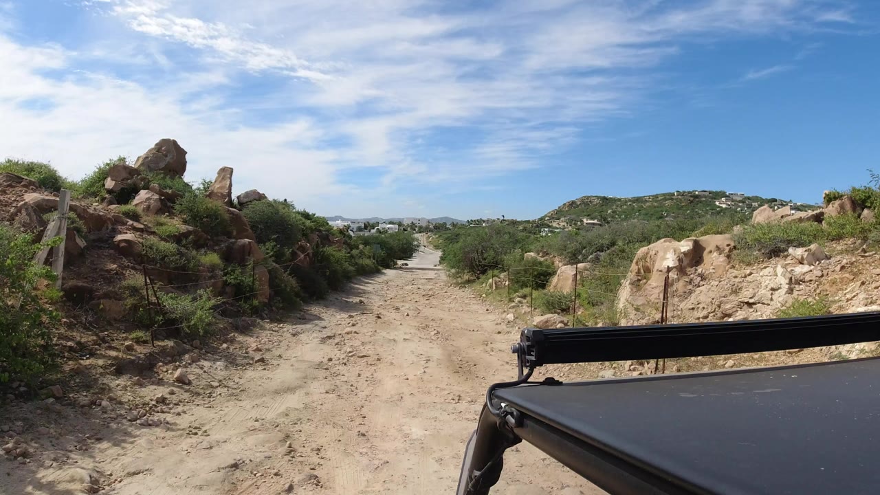 Dusty road beside rocks and shrubs with a cart roof in the foreground.