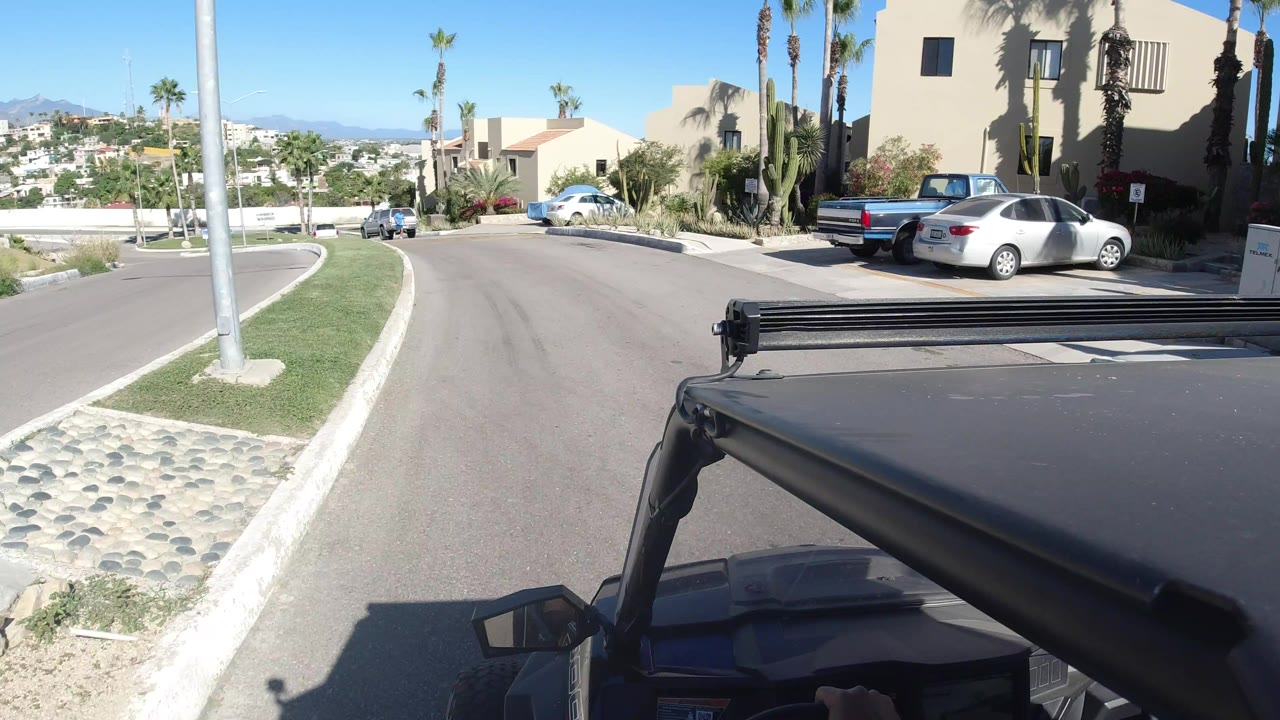 Second frame shows the Los Cabos road curving left past a grass strip and desert planting, with parked cars near stucco buildings and no visible people.