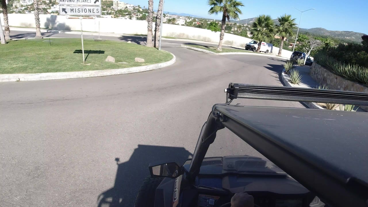 Wrangler hood view on a curving road with palm trees and a sign.