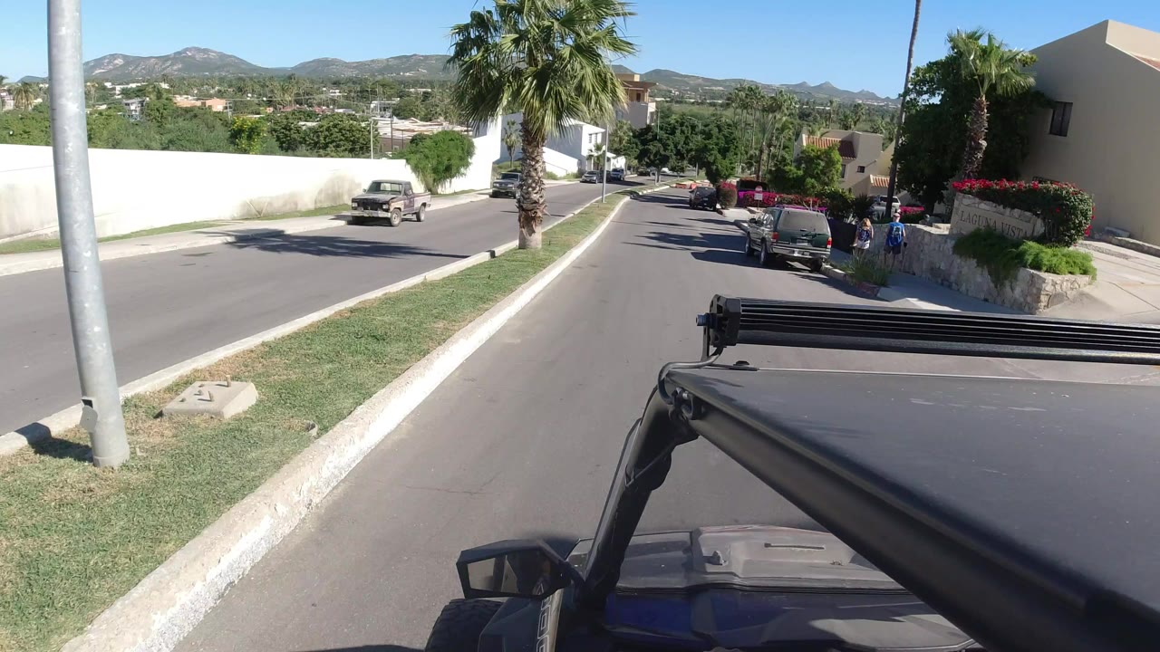 Jeep foreground on a sunny residential road with palm trees and white buildings.