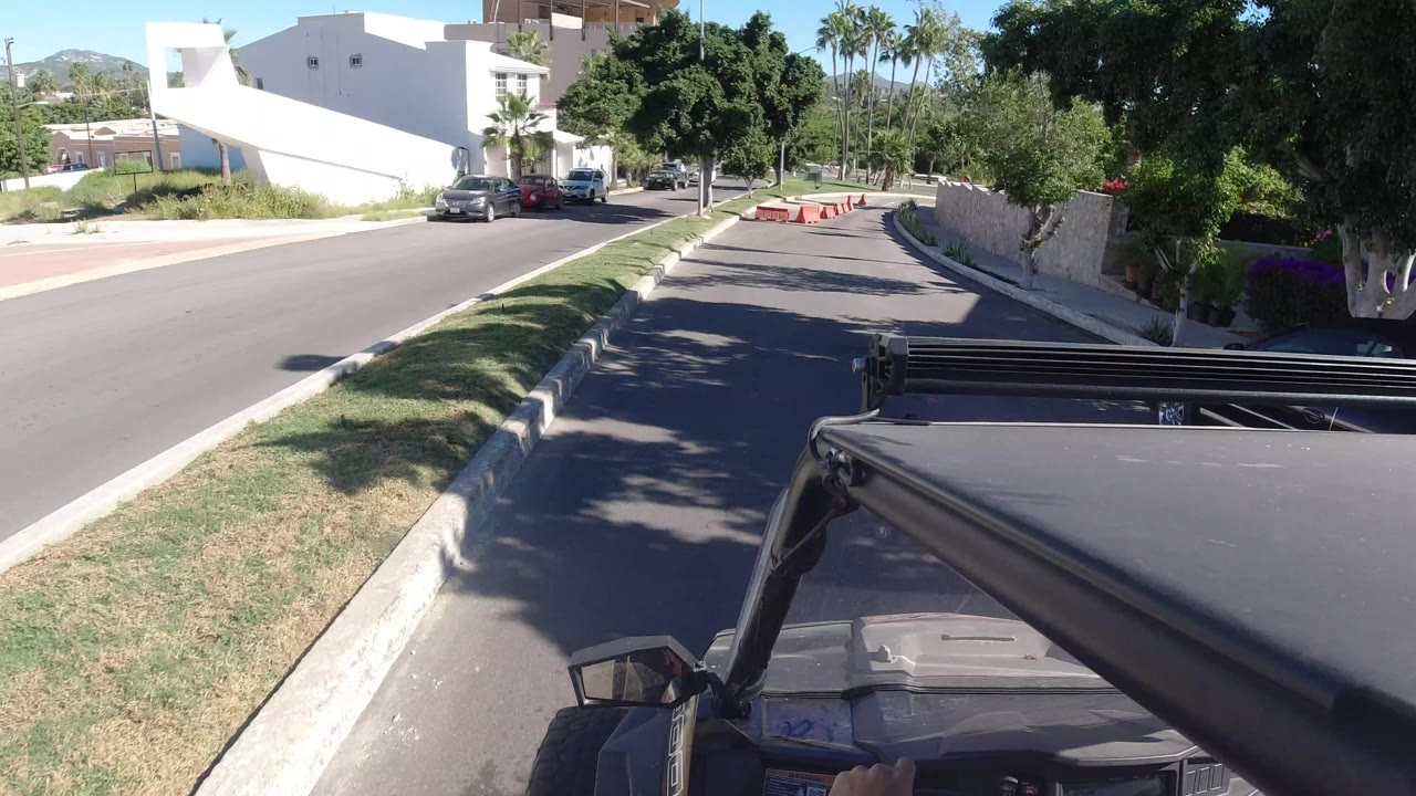 Vehicle hood approaching a quiet divided street with orange barricades ahead.