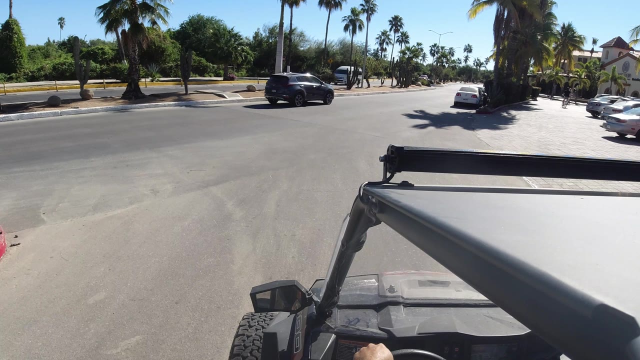 Wide road view from Jeep with parked cars and palms