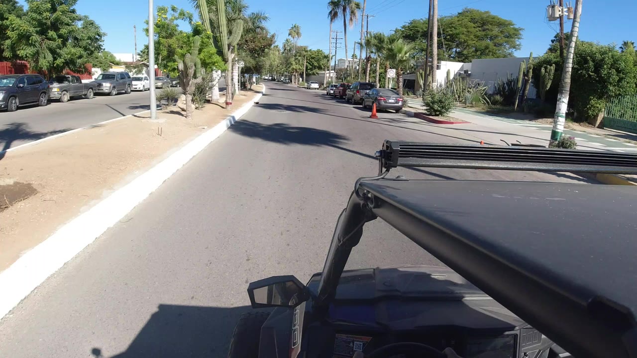 Vehicle POV on a sunny road with palms and parked cars