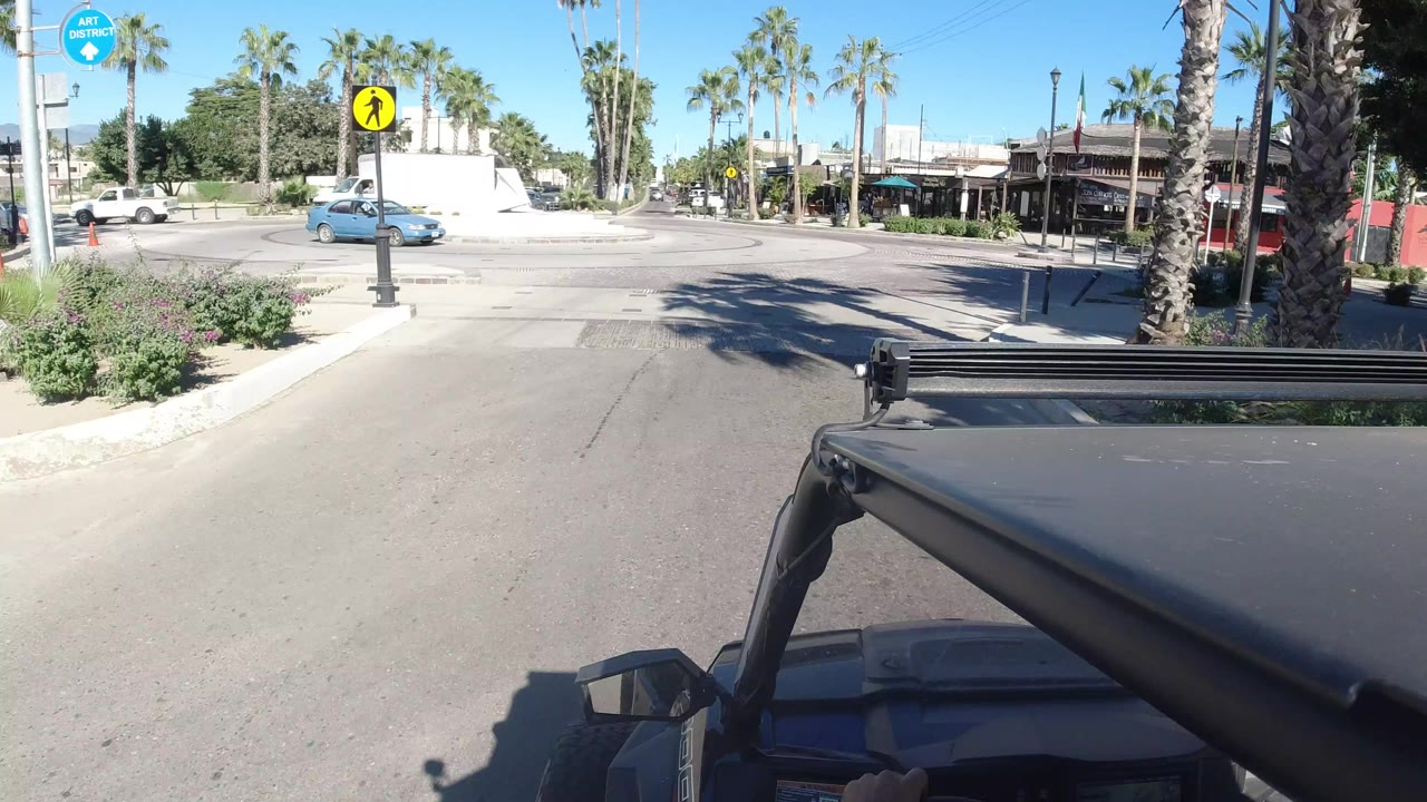 Vehicle hood facing a palm-lined intersection with cars and storefronts