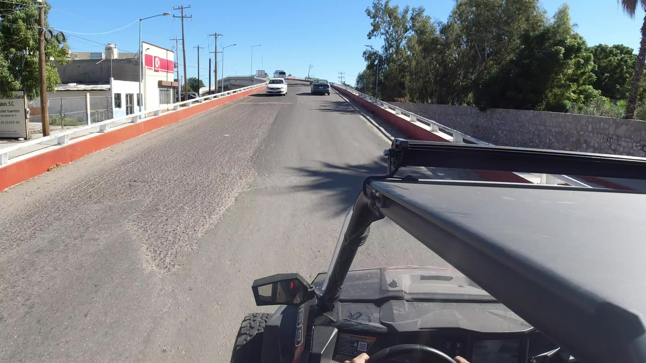 Vehicle POV on a narrow bridge road with cars ahead and trees beside it.