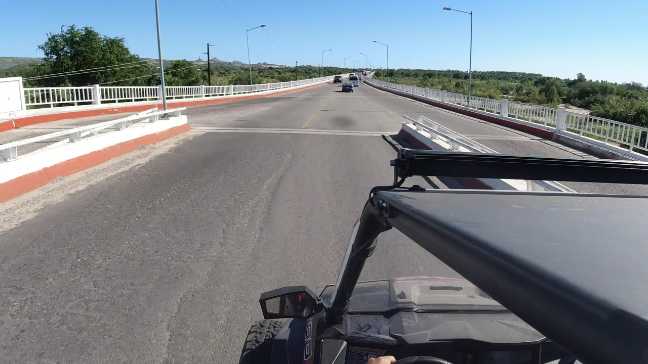 Forward road view from an open vehicle on a bridge with white railings.