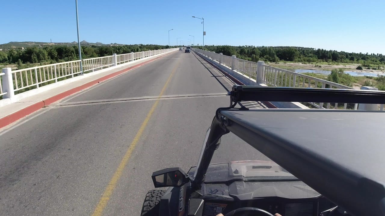 Forward vehicle view on a bridge road with white railings and cars ahead.