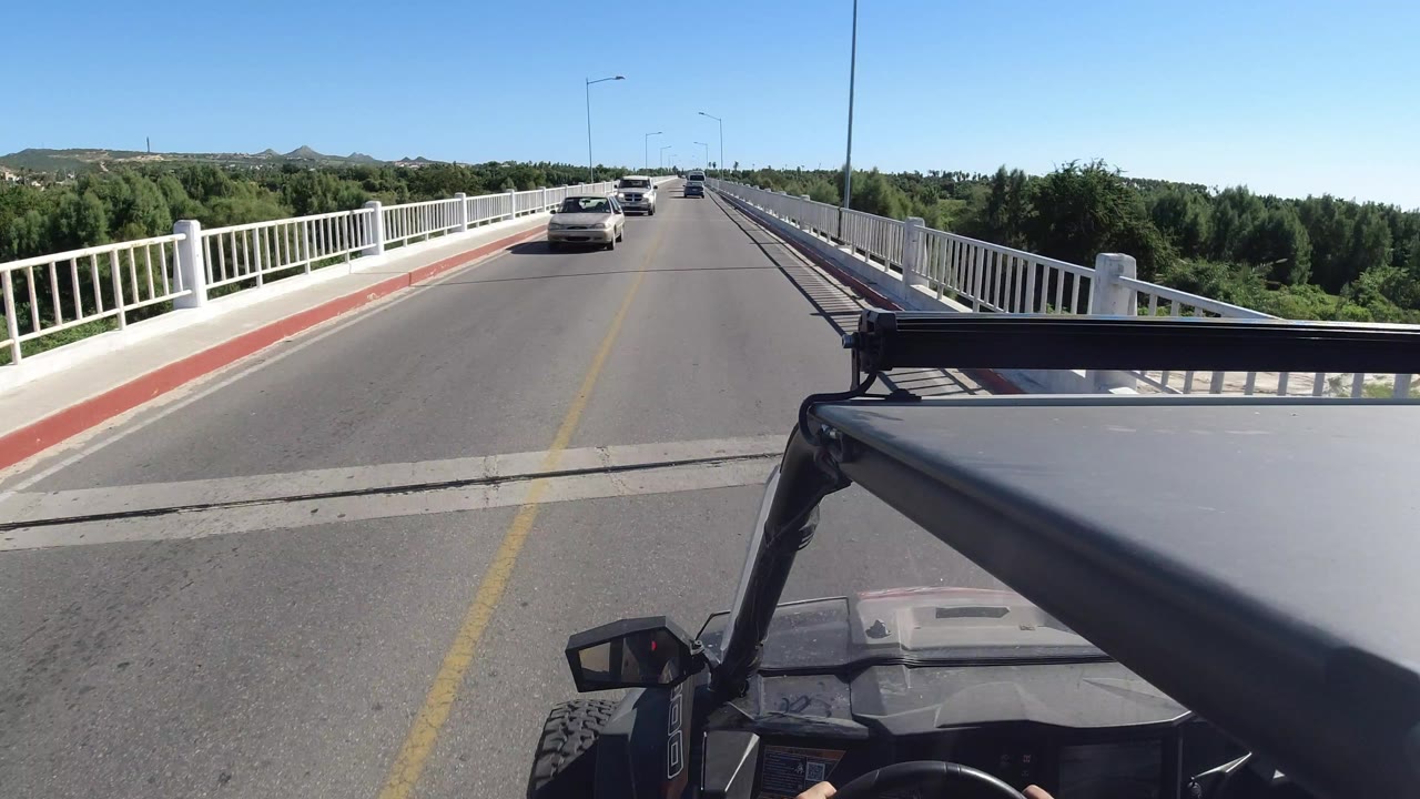 Open vehicle view on a bridge road with a car approaching ahead.