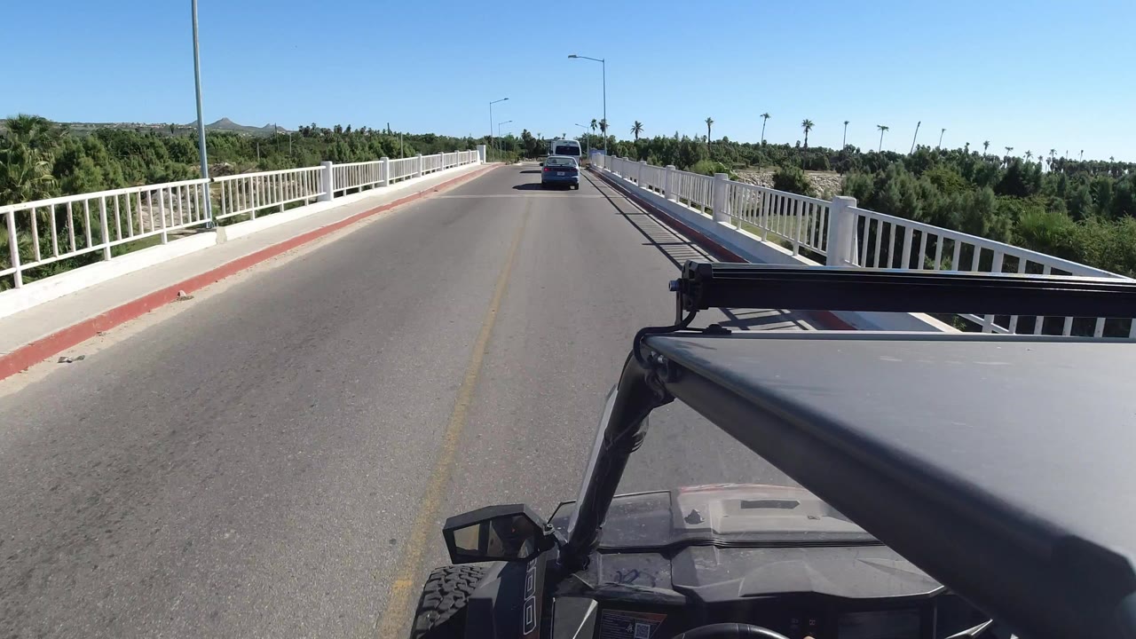 Vehicle POV on a bridge road under blue sky.