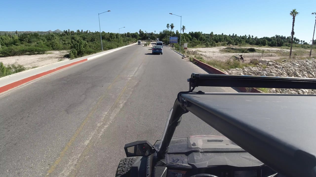 Roadway from a Wrangler with roadside vegetation, palms, and a vehicle ahead.