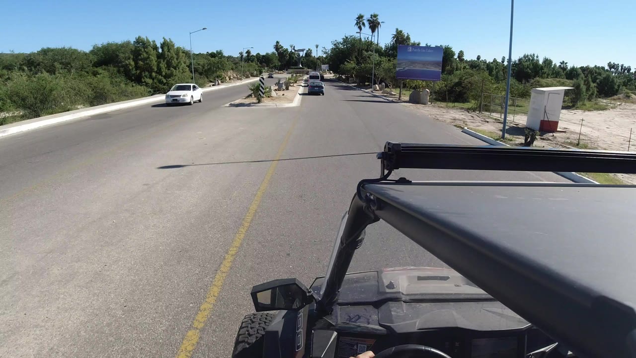 Open vehicle view down a sunny road with cars ahead and desert landscaping.