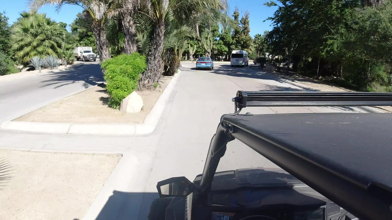Roof-mounted Jeep view on a divided road with palm landscaping and vehicles ahead.