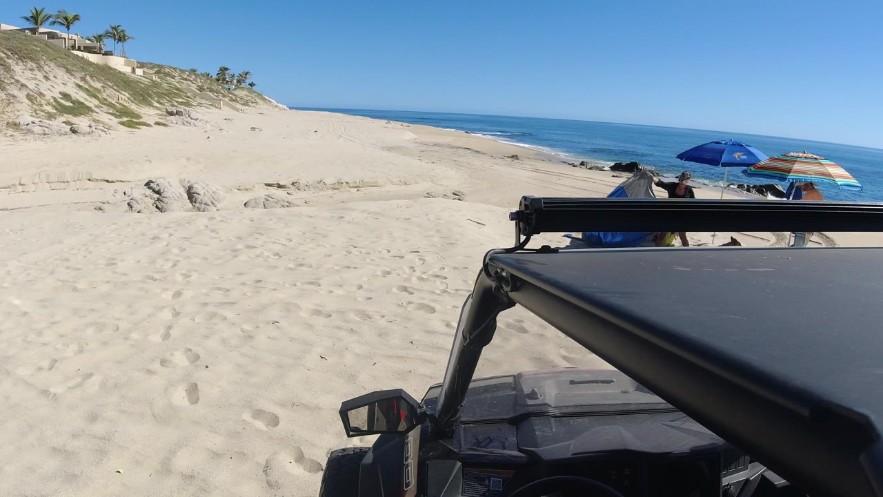 Beach dunes, ocean, umbrellas, and a vehicle roof in the foreground.