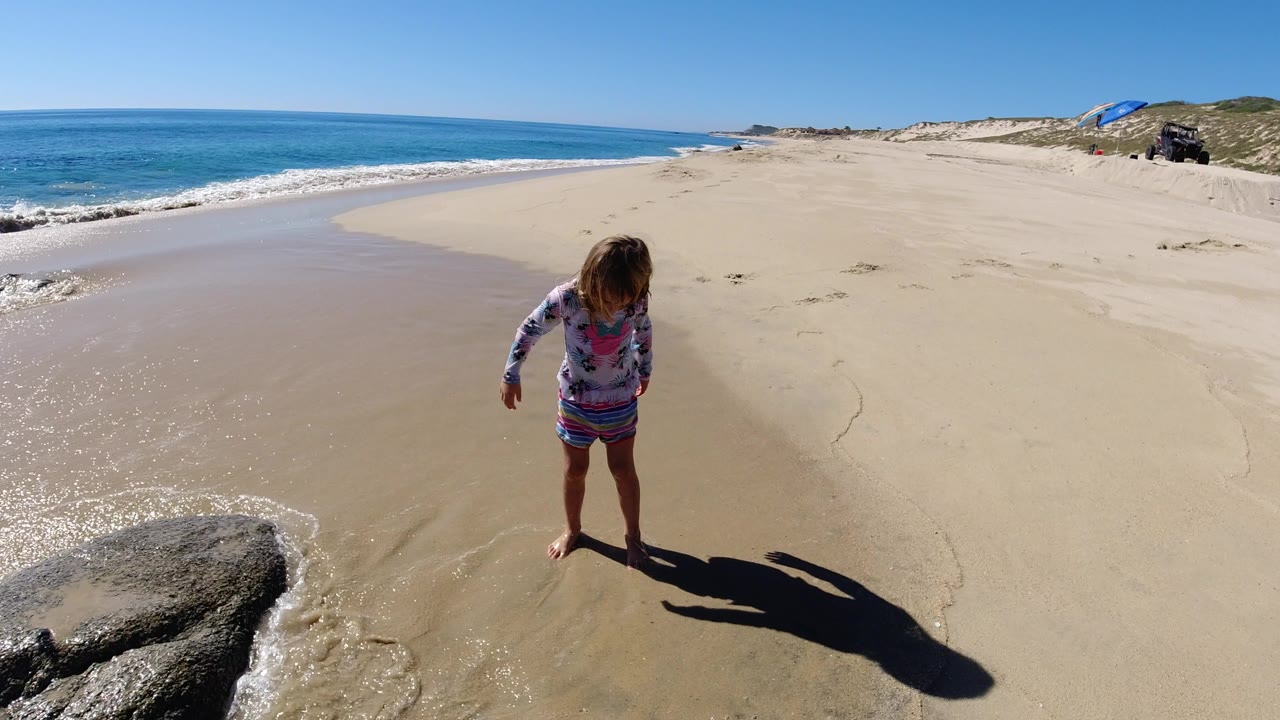 Young child standing barefoot on wet beach sand near ocean waves.