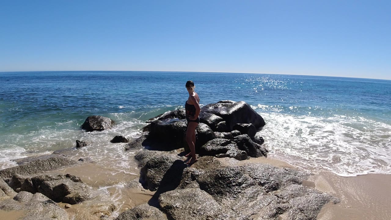 Adult woman standing on beach rocks beside the ocean