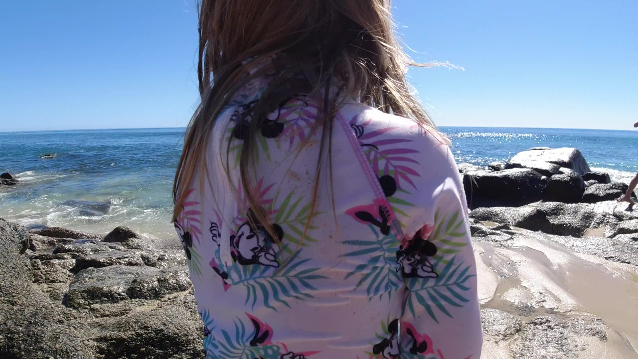 In Los Cabos, Mexico, the child remains close to camera with wet rocks and sunlit ocean water stretching across the background.