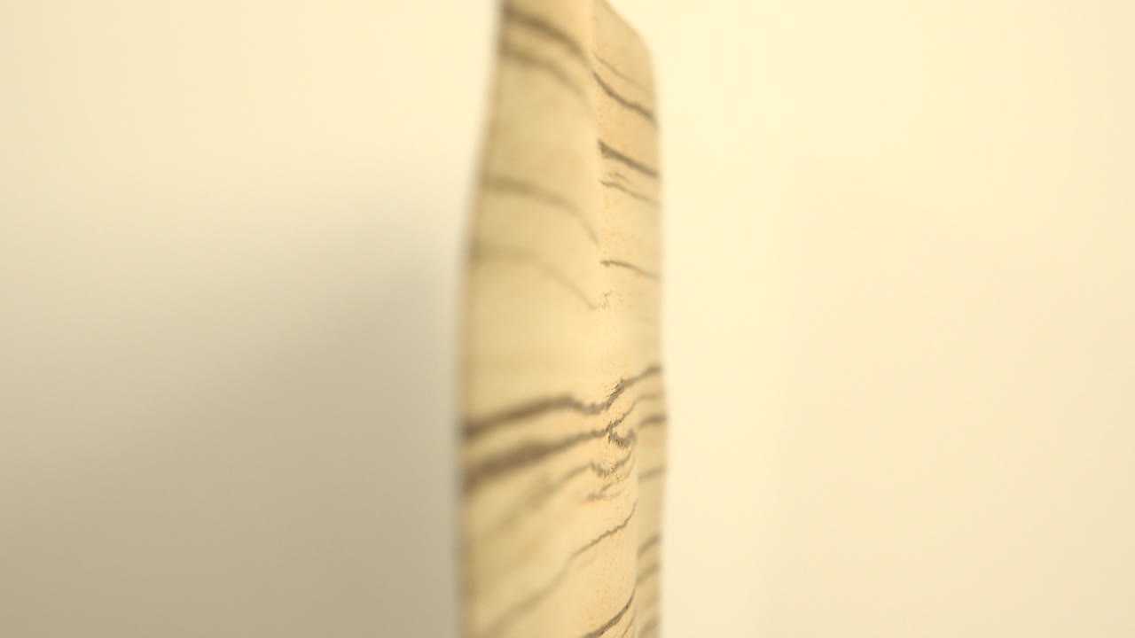 A shallow-focus close-up shows the edge of a pale striped wooden board between soft white curved surfaces, with no visible people.