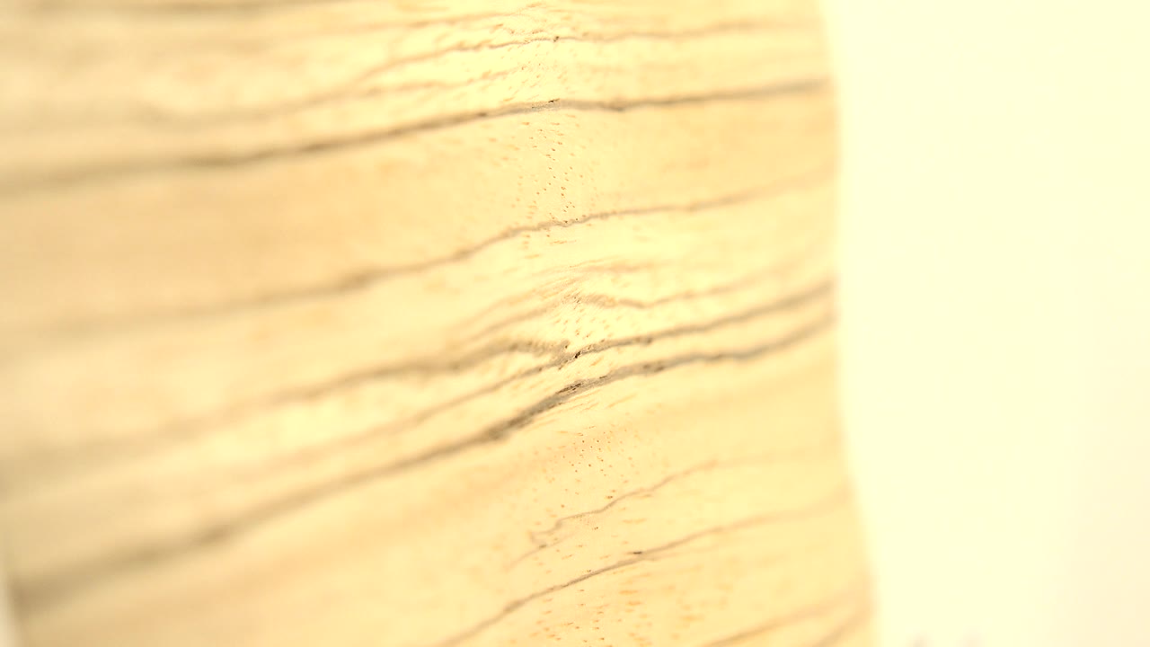 A close view of the wooden board shows dark grain lines slanting across the pale surface with a white background strip near the right edge and no visible people.