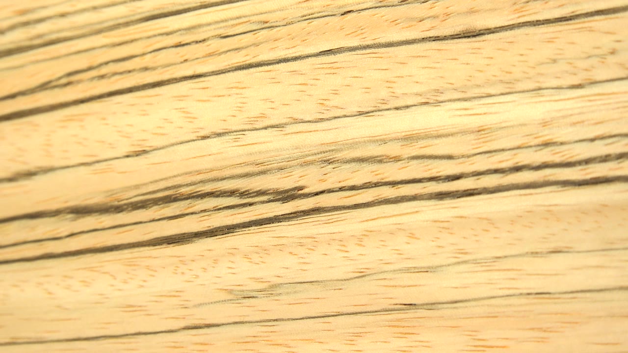A close-up of pale wood grain stretches diagonally across the frame under warm light, with no visible people.