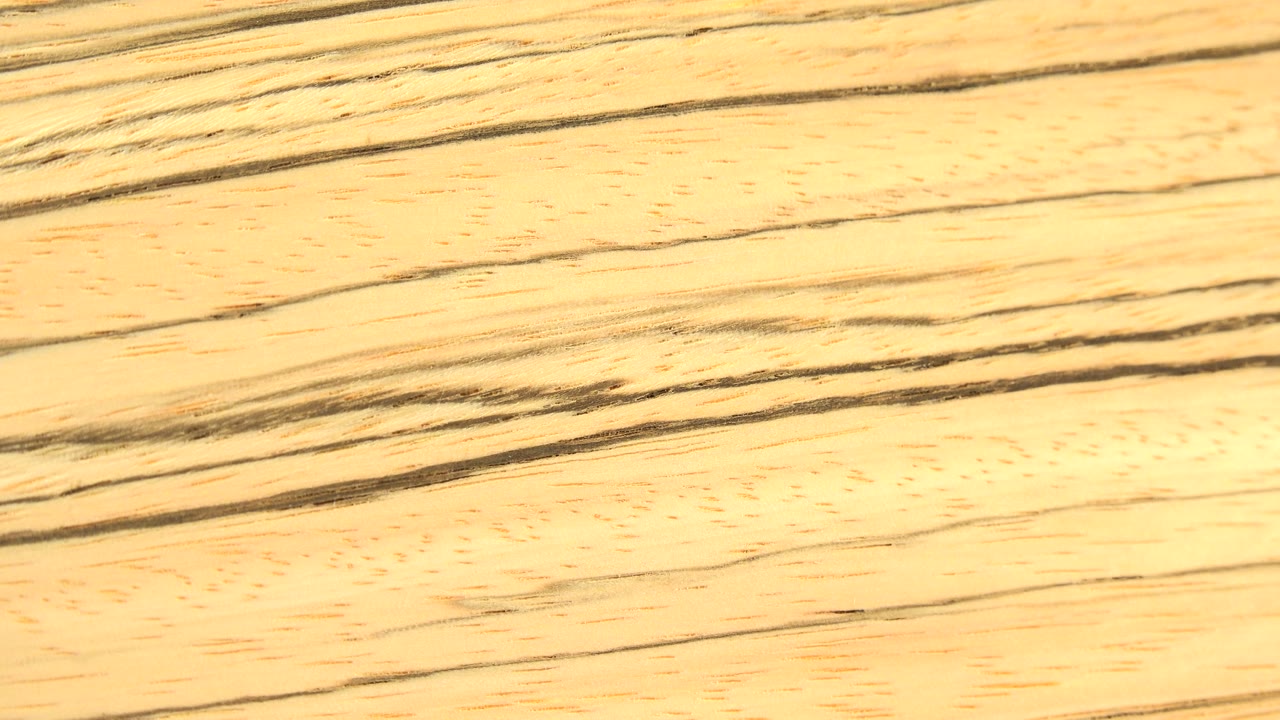 A brighter section of pale wood grain fills the frame, with thin dark streaks and warm yellow highlights, and no visible people.