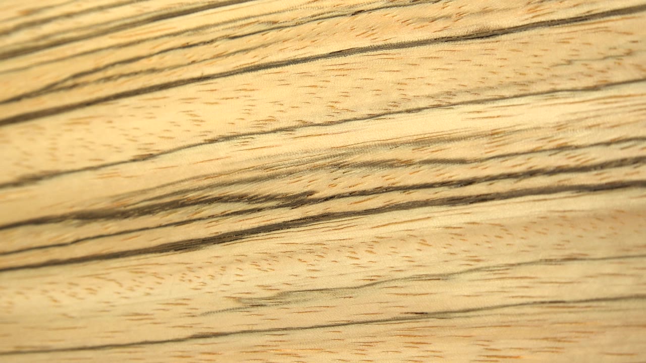 A closer, sharper section of pale flat wood fills the frame with dark flowing grain lines and small speckled pores, with no visible people.