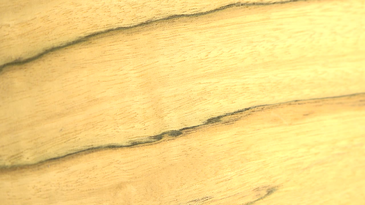 Close-up of pale yellow wood grain filling the frame, with dark uneven horizontal lines and no visible people.