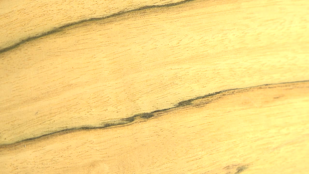 A close frontal view of pale golden wood texture with dark uneven grain lines crossing the frame and no visible people.