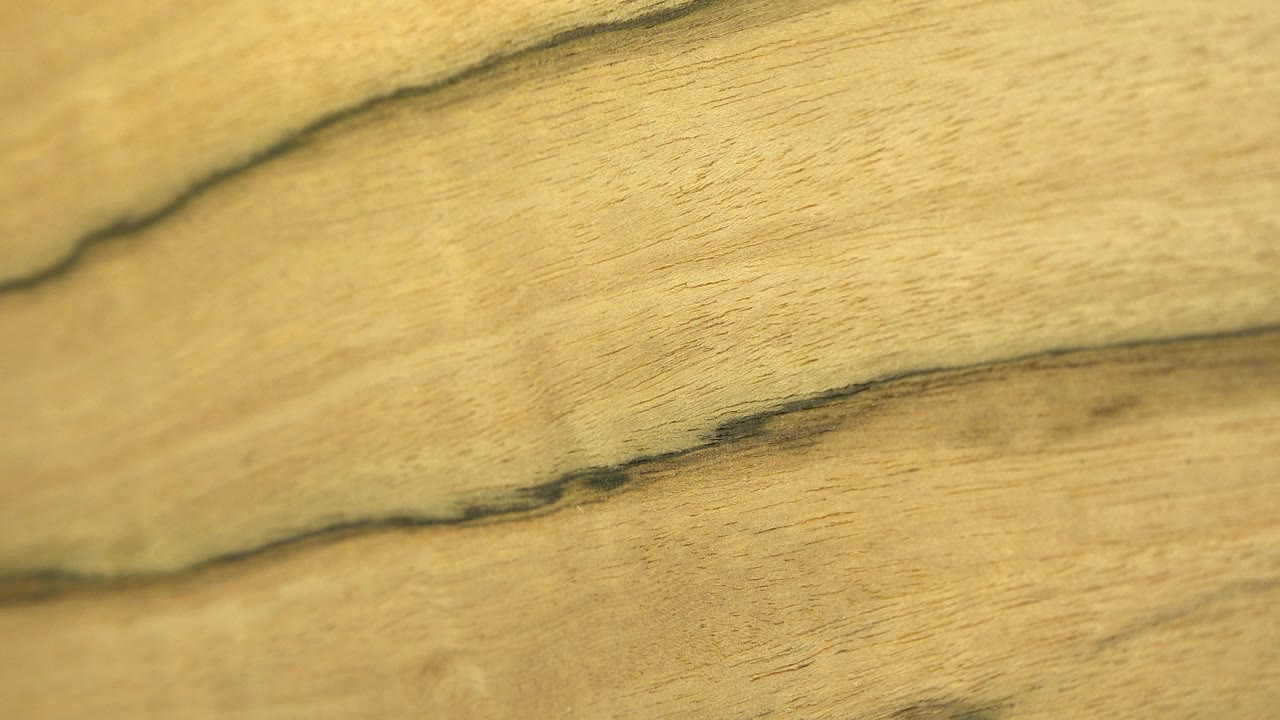 Sharper close-up of yellow-toned wood with two dark, uneven grain lines crossing the frame, with no visible people.