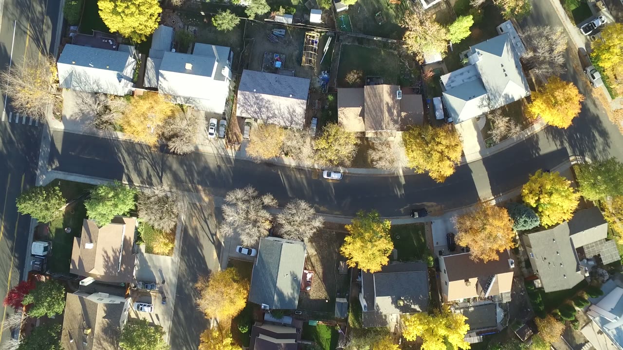Overhead aerial frame of Hidden Lake, Colorado showing detached homes, fenced yards, residential streets, parked cars, and yellow-green tree canopies with no visible people.
