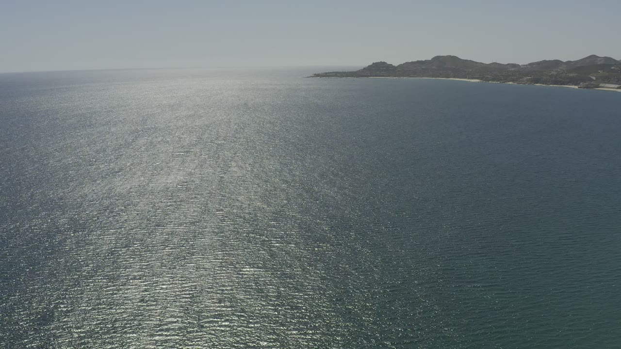 Wide aerial view over sunlit ocean toward a distant coastline.