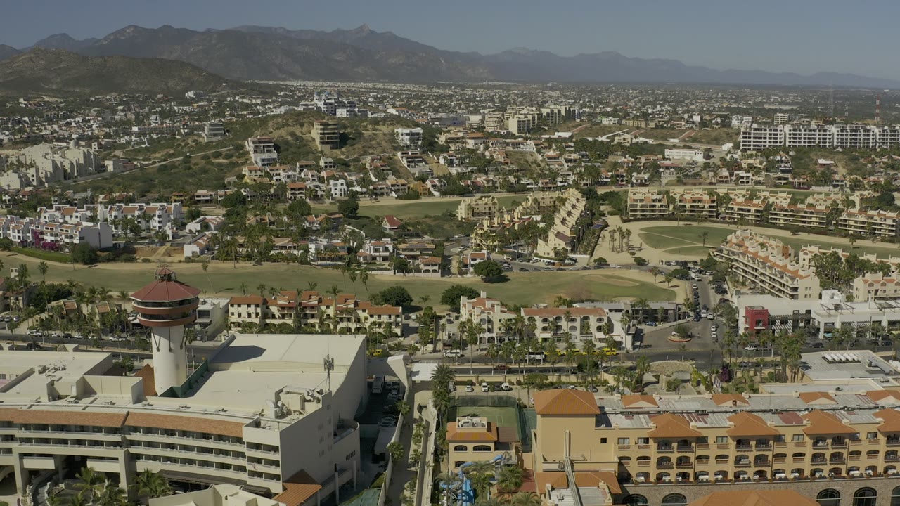 Aerial view of hillside buildings, roads, green areas, and distant mountains.