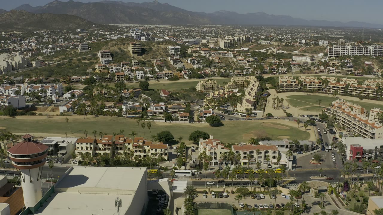 Elevated town view with green fairway-like grounds, roads, buildings, and mountains.