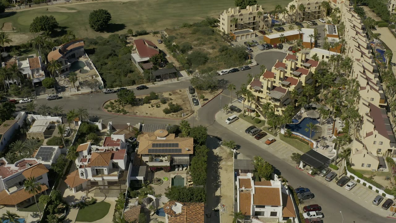 Aerial view of villas, roads, pools, parked cars, palms, and green space.