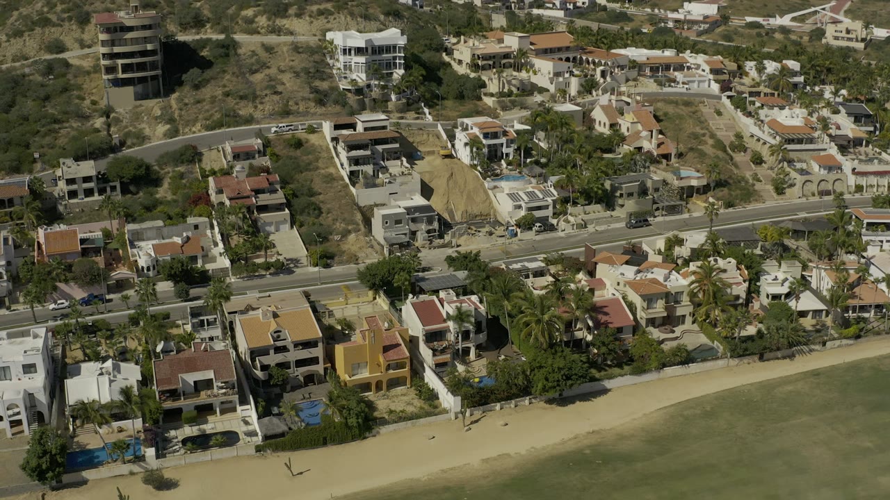 Aerial view of hillside homes beside a road and sandy beach area.