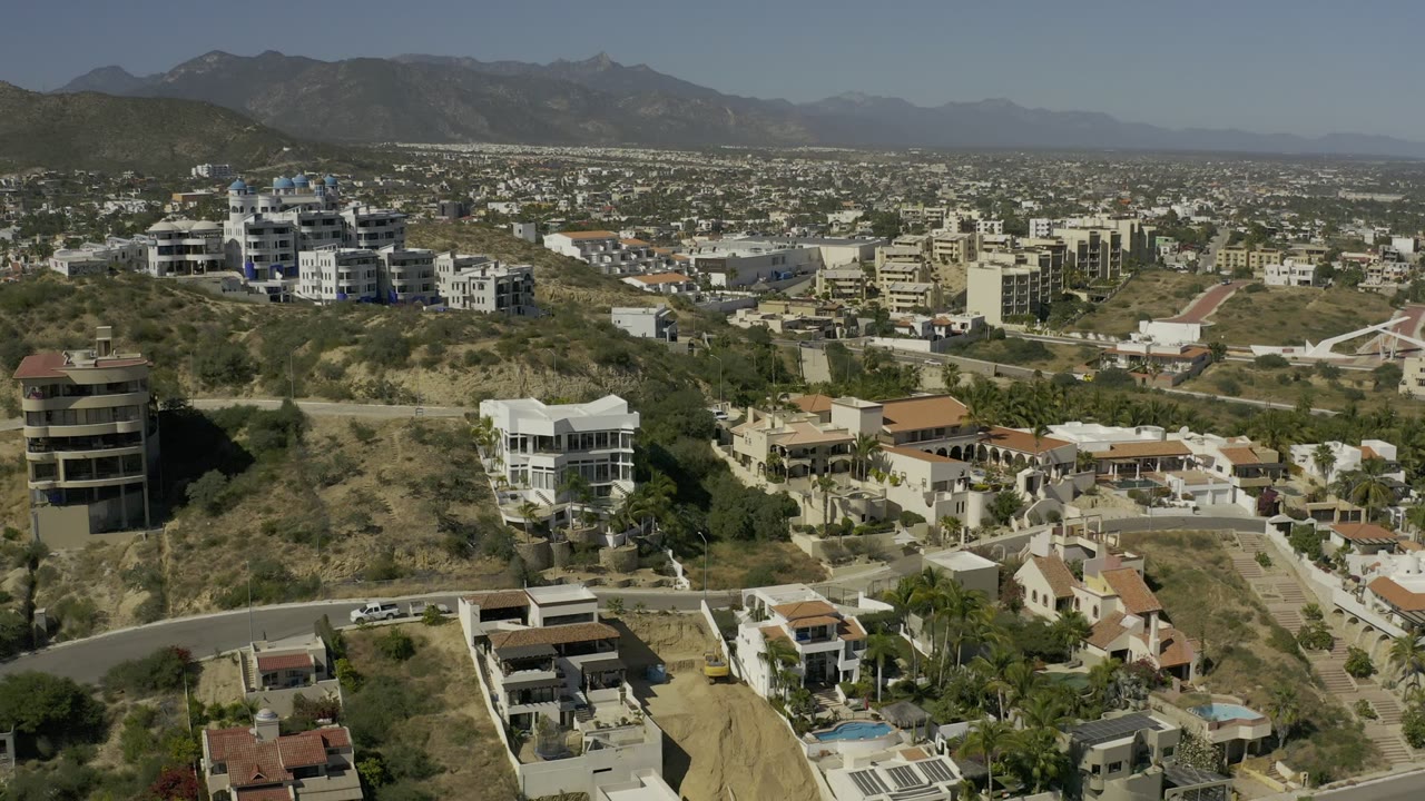 Aerial view of hillside homes, roads, city buildings, and mountains.