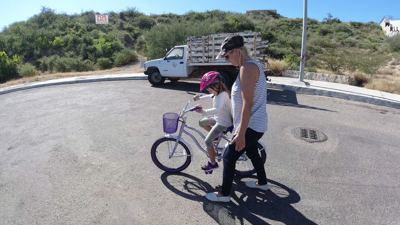 Woman walking beside a child riding a small bicycle on a paved street.