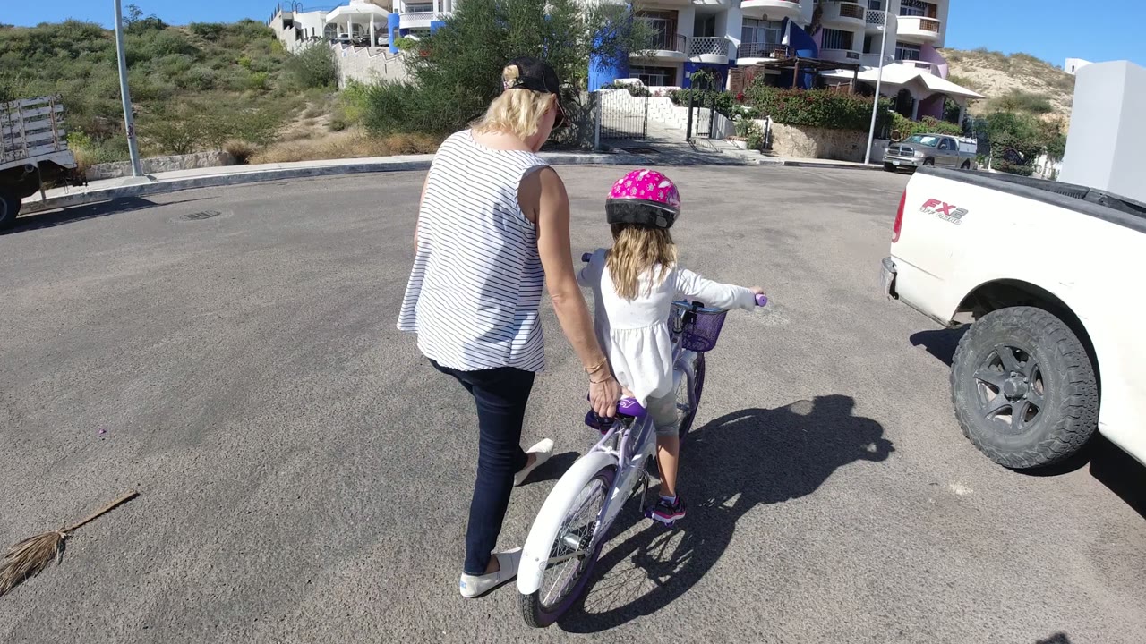 Woman helping a child on a small bicycle on a quiet paved road.
