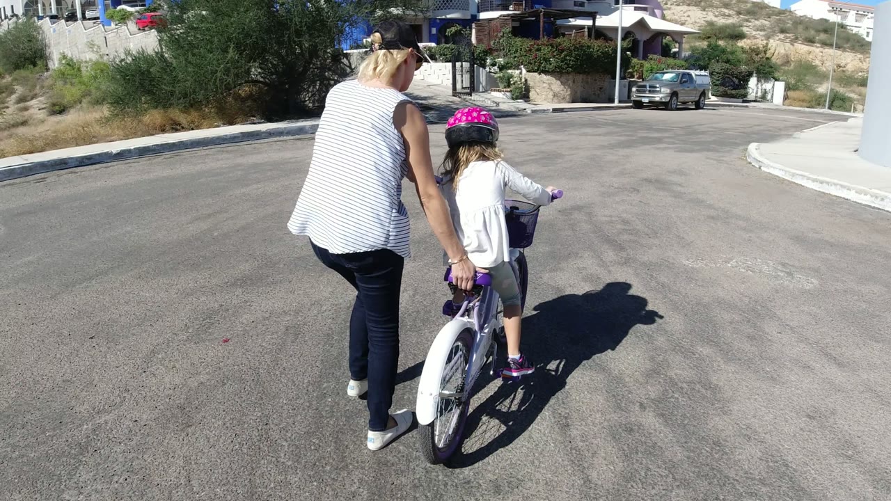 Woman walking beside a child on a bicycle in a sunny street.