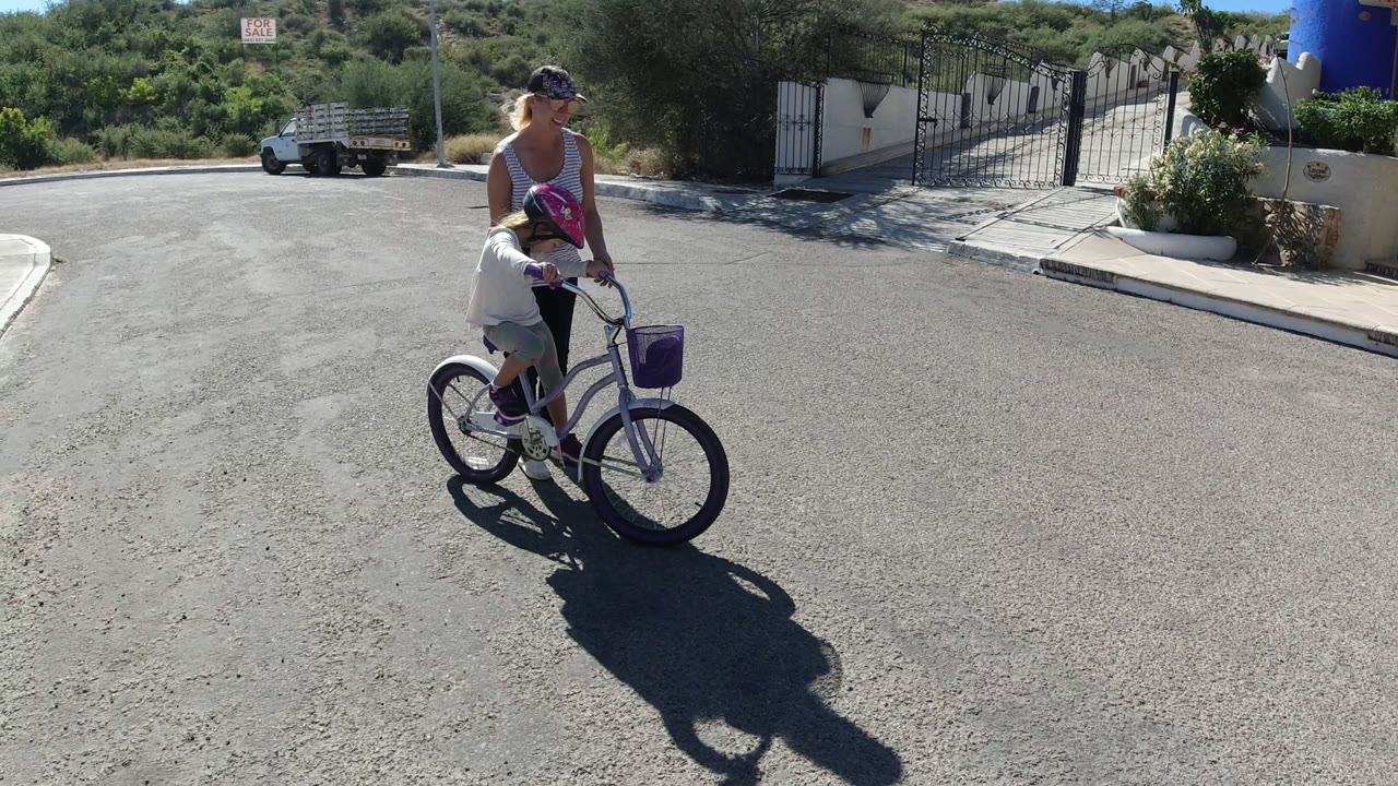 Woman guiding a child on a small bicycle in a sunny street.