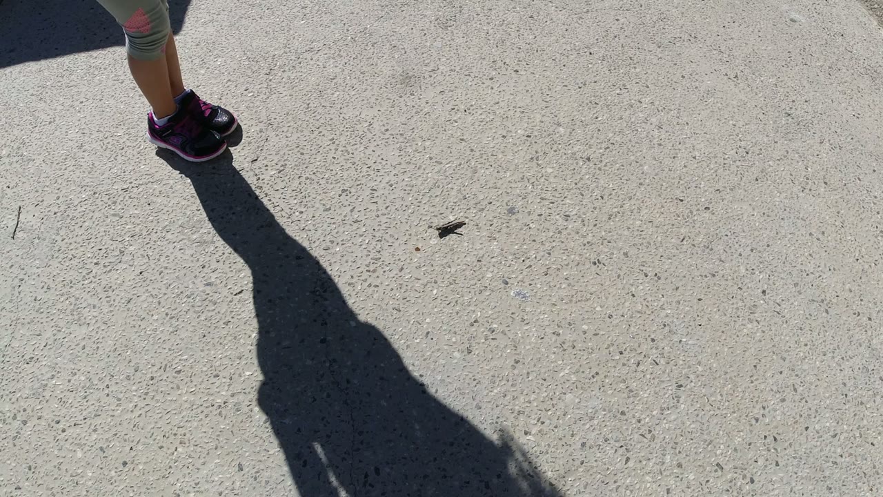 At 0:01 in San Jose del Cabo, the child's shoes sit near the upper frame while the shadow extends down the center of the concrete surface.