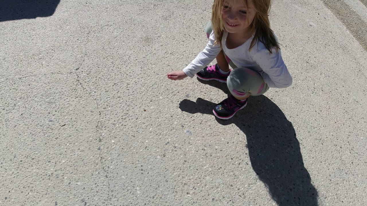 Young girl crouching on sunlit pavement with a long shadow.