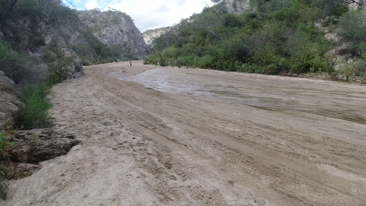 Wide dirt wash curving between rocky hills and green brush.