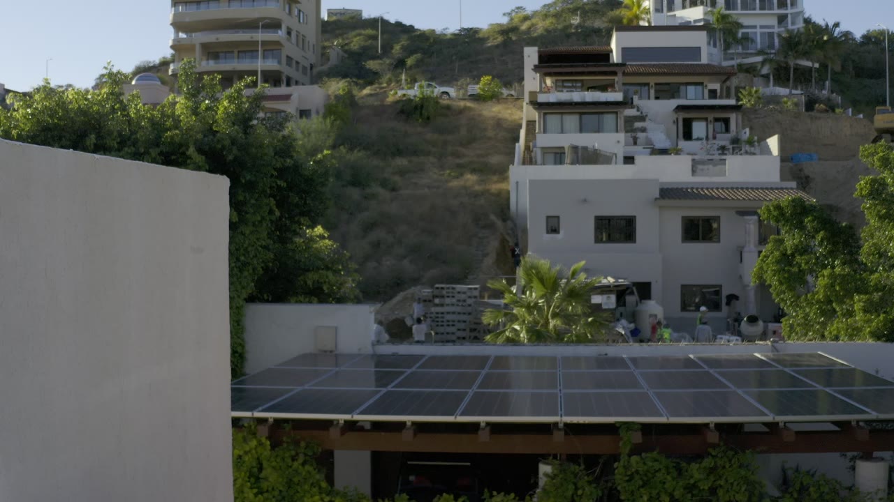 Second frame shows the same Los Cabos hillside residences, with white walls, shaded trees, dry slope vegetation, and no visible people.