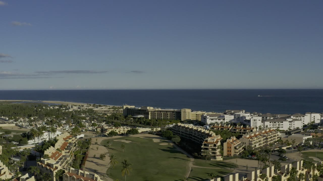 Aerial view of coastal buildings, green grounds, and ocean horizon.