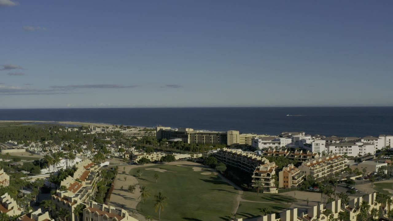 Elevated coastal view with resort buildings, green grounds, beach, and ocean horizon.