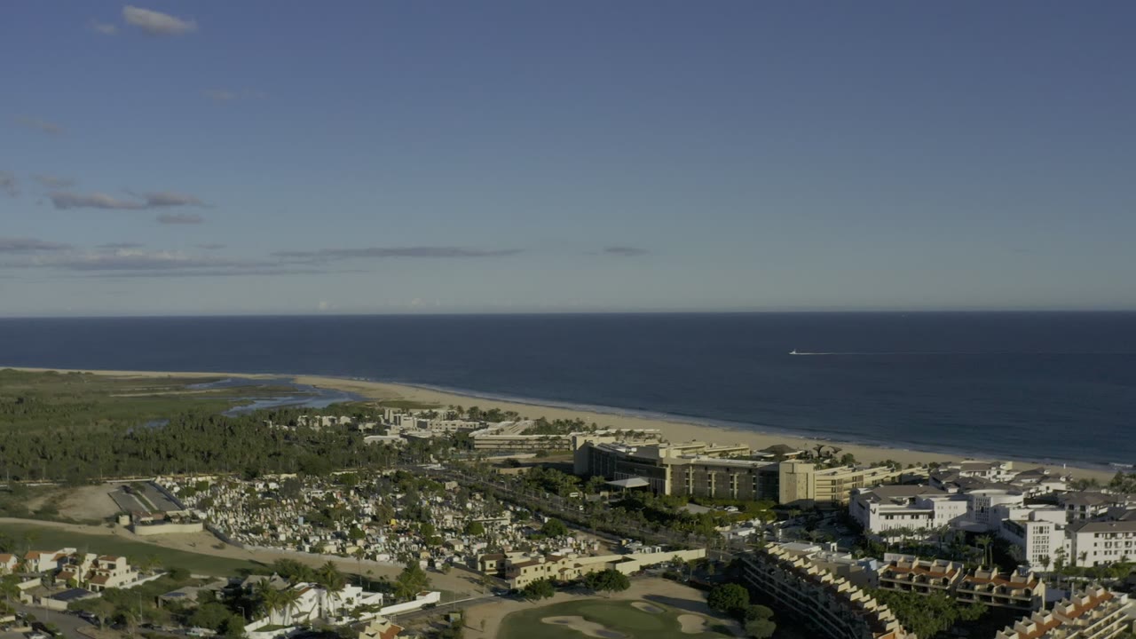 Aerial coastal view with buildings, beach, ocean, and clear sky.