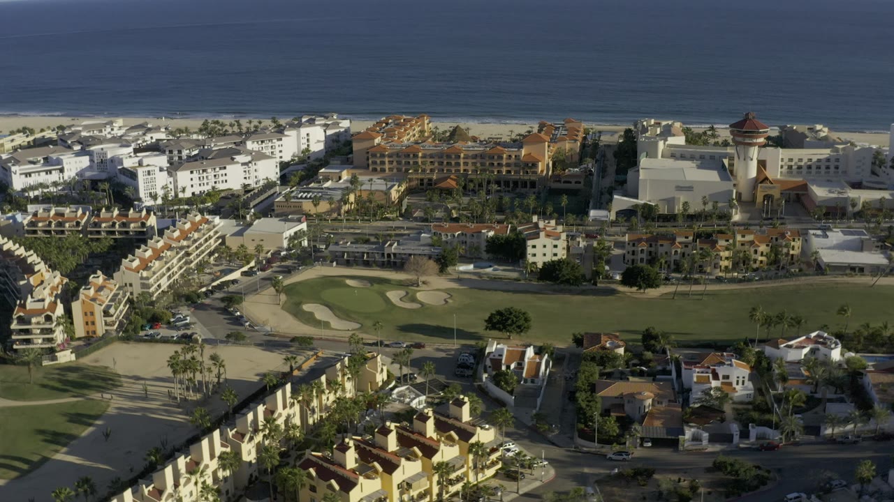 Elevated coastal view with golf fairway, sand traps, buildings, beach, and ocean horizon.