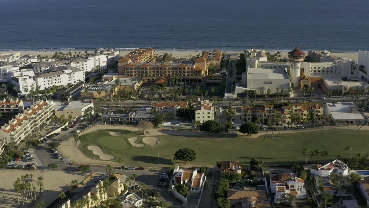 Aerial view of coastal town buildings, roads, green grounds, and ocean.